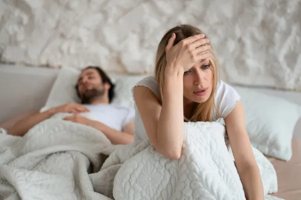 Woman looking frustrated in bed next to partner, symbolizing libido and intimacy challenges