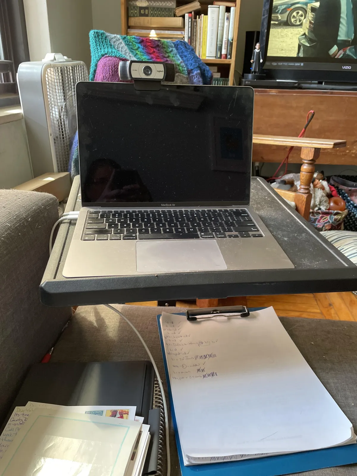 An powered down laptop is open on a small black table between a couch and a TV. 