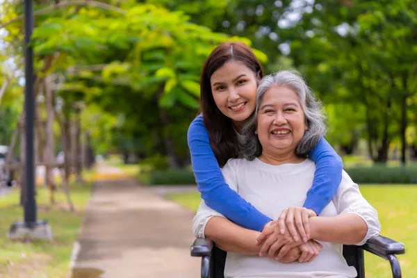 Daughter hugging elderly mother in wheelchair, showing love and caregiving support.
