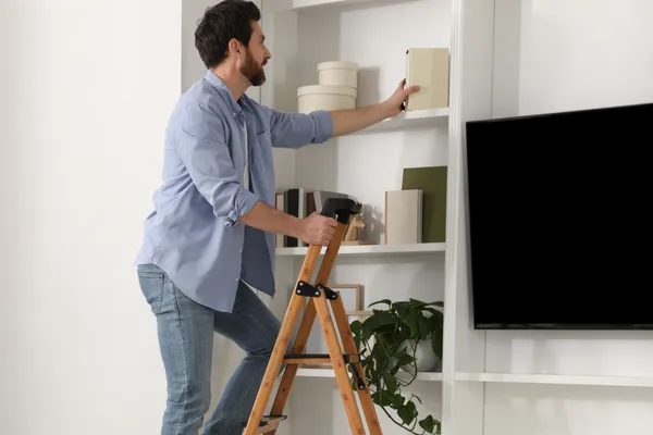 Man standing on a step ladder in a home setting, emphasising safe practices to reduce the risk of falls and brain injury.