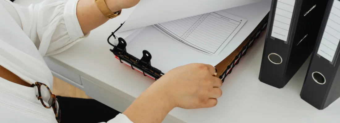 Professional preparing and filing ISED certification documents in binders for regulatory record keeping.