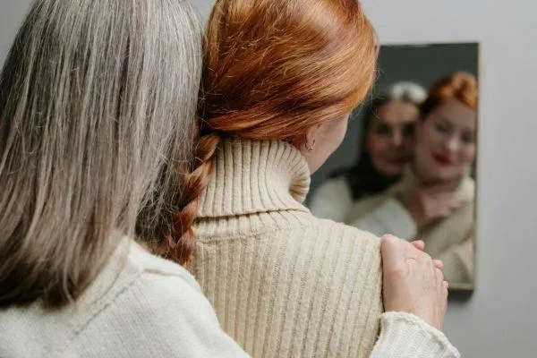 A mature woman in her 50s standing beside a younger woman, both gazing into a mirror—symbolising reflection, generational connection, and rediscovery after divorce.