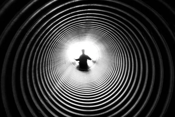 Person walking out of a dark tunnel into bright light, symbolising healing from trauma, moving through triggers, and stepping into empowerment and freedom.
