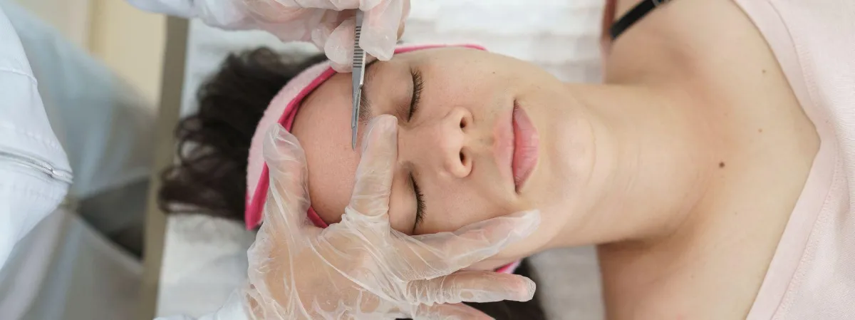 Close-up of a professional dermaplaning session, showcasing a gloved aesthetician gently exfoliating a client's face with a specialized blade, highlighting the smooth and precise technique used to enhance skin texture and glow.