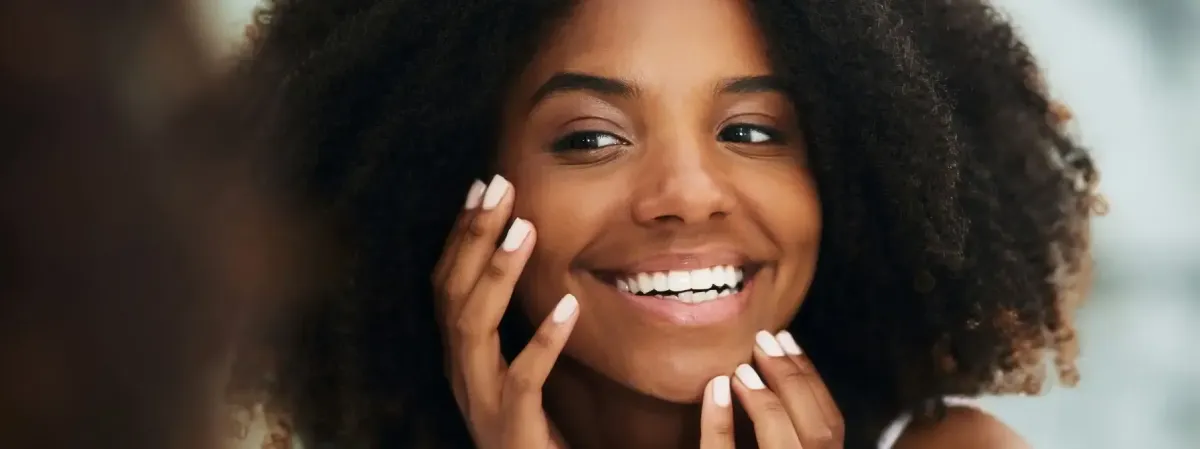 Smiling woman with glowing, smooth skin gently touching her face, reflecting the rejuvenating results of a chemical peel treatment in Greenville, SC.