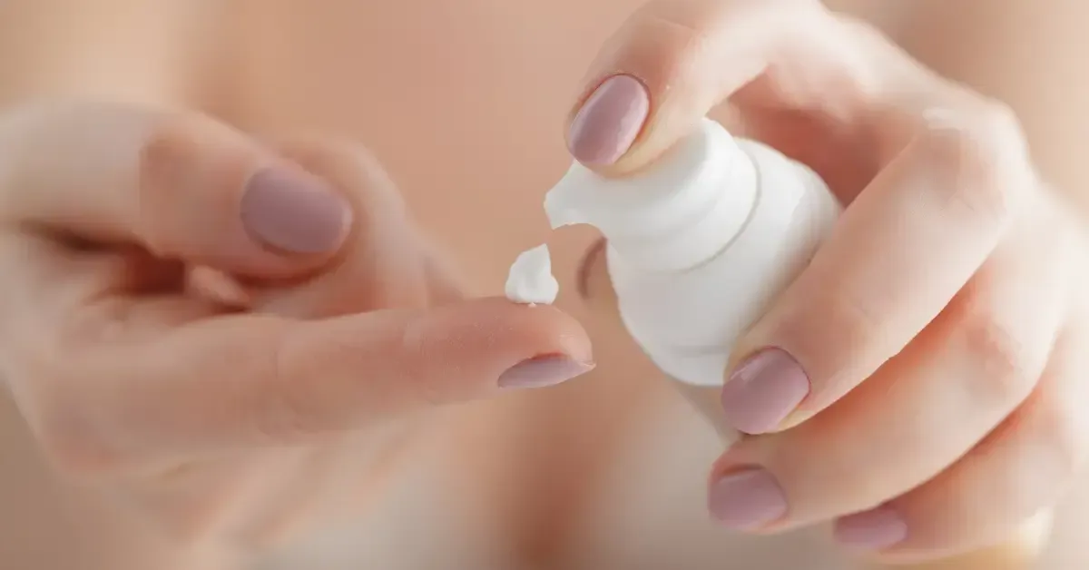 Close-up of a woman dispensing a small amount of moisturizer onto her fingertip