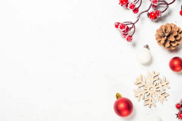 Festive Christmas decorations arranged on a white marble surface, featuring frosted red berries, a pine cone, red and white ornaments, and a wooden snowflake. The decor lines the right and bottom edges, leaving ample blank space on the left.