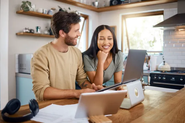Couple planning a last-minute trip on a laptop at home, comparing travel options together.