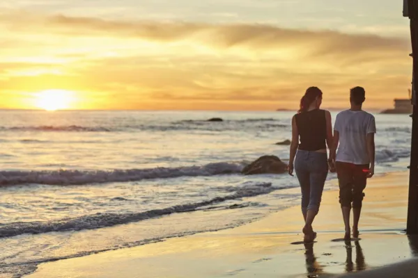 Couple walking along the beach at sunset, enjoying a peaceful warm-weather getaway.