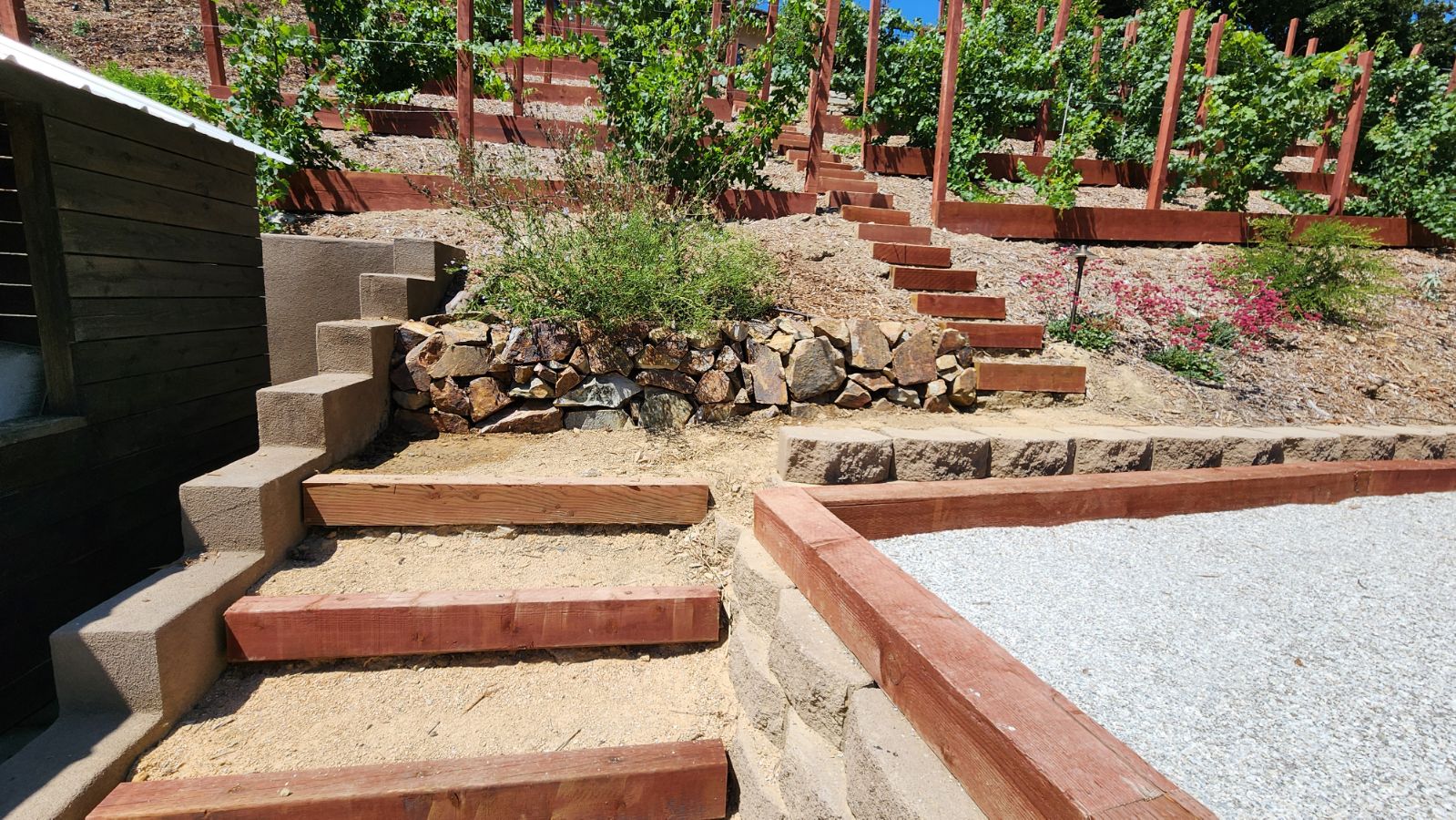 Tiered timber garden steps and stone retaining walls on a steep hillside.