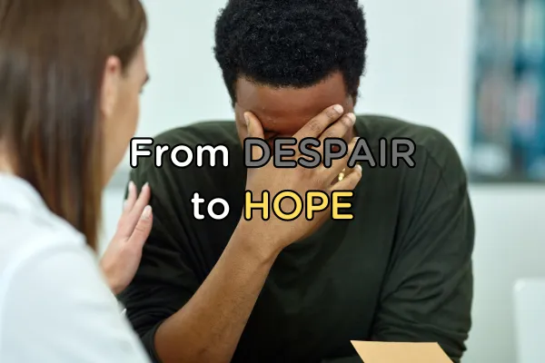 A young man in distress sits with his face in his hands, he is being comforted by a female friend