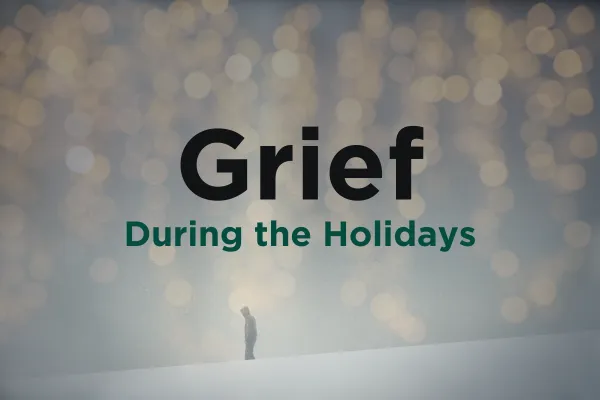 Grief during the holidays. A person stands alone amidst snow and holiday lights