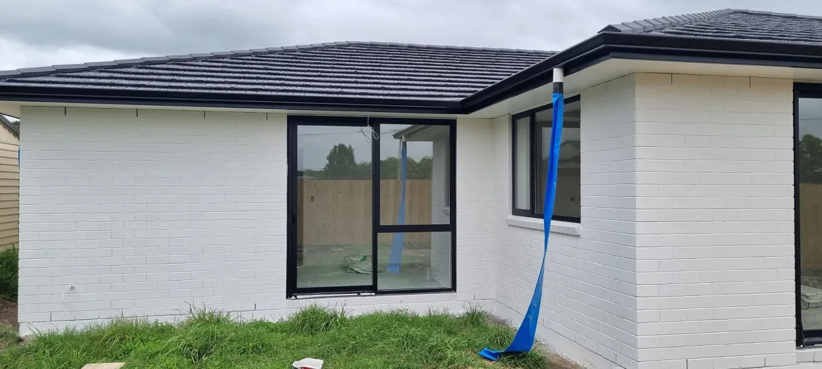 White painted brick house exterior with black window trim and drop sheet setup visible