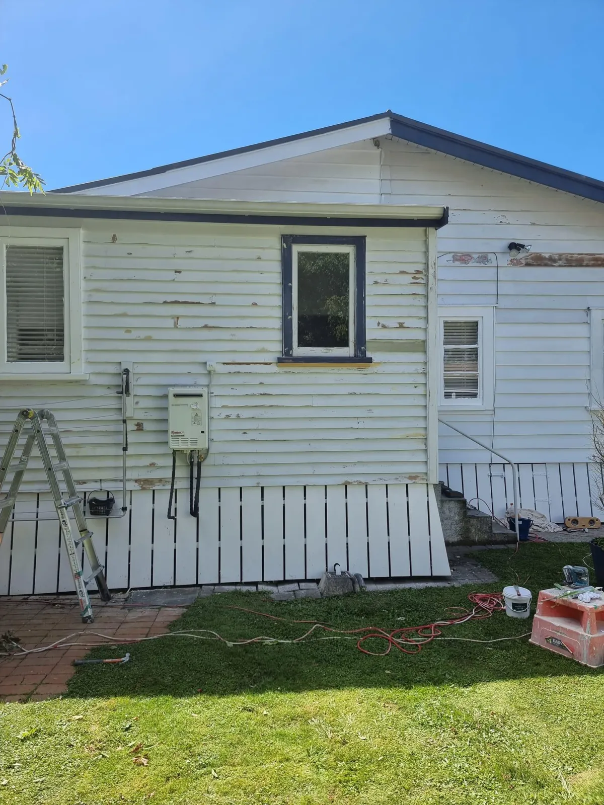 Weatherboard home in Hamilton mid-renovation with patchy old paint and ladders ready