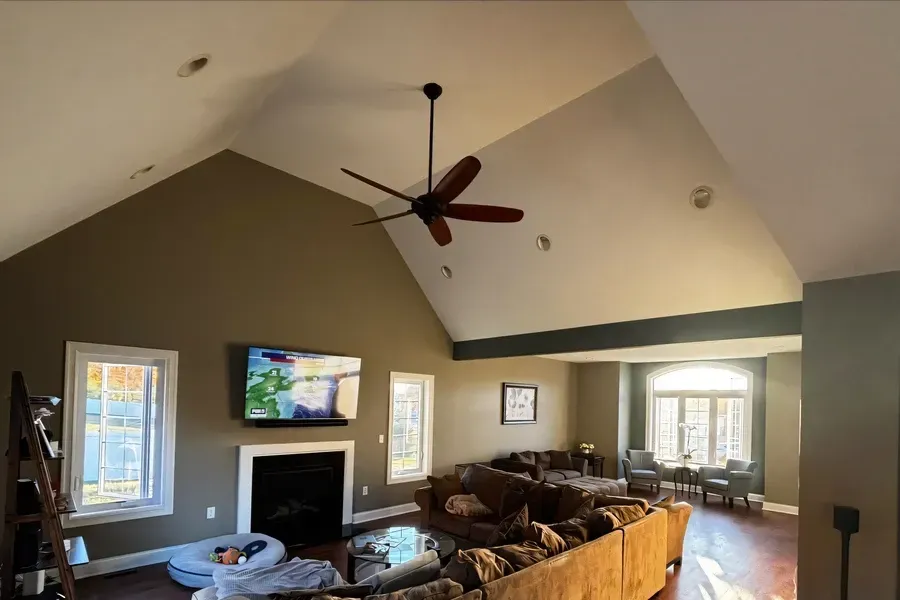 Spacious living room in Hamilton, NJ with vaulted ceilings, olive green accent walls, a ceiling fan, and a mounted TV above a fireplace, showing a recent professional paint job.