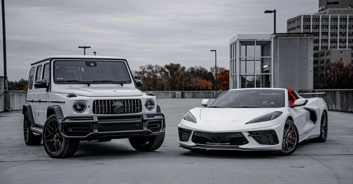 White Mercedes-Benz G-Class SUV parked on a city street with modern skyscrapers and autumn trees in the background