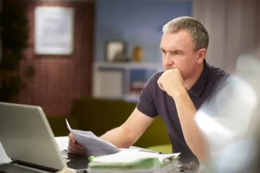 A small business owner overwhelmed with paperwork and resumes at their desk, symbolizing hiring stress and the need for better hiring strategies.