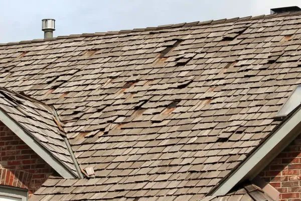 A close-up view of a roof with extensive hail damage, featuring numerous cracked and missing shingles on a residential home.