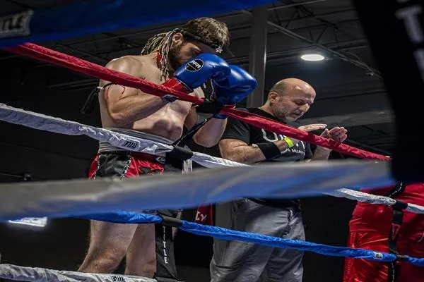Fighter and coach bowing their heads on the ring ropes in a ritual prayer, resembling the Wai Kru Ram Muay tradition, symbolizing respect, focus, and unity before the fight.