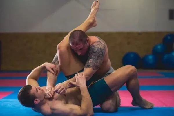Two beginners practicing grappling techniques on a padded mat in a well-lit professional training facility, emphasizing foundational skills and proper form.