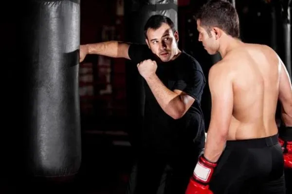 A coach guiding a fighter during training near a punching bag, showcasing preparation and discipline for professional fighting.