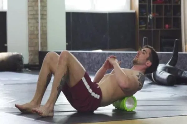 A fighter using a foam roller on a gym mat to release tight muscles and enhance recovery during fight preparation.