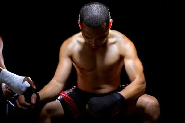 A fighter seated with head bowed and hands wrapped, appearing to pray or mentally prepare for a fight in a focused and reflective moment.