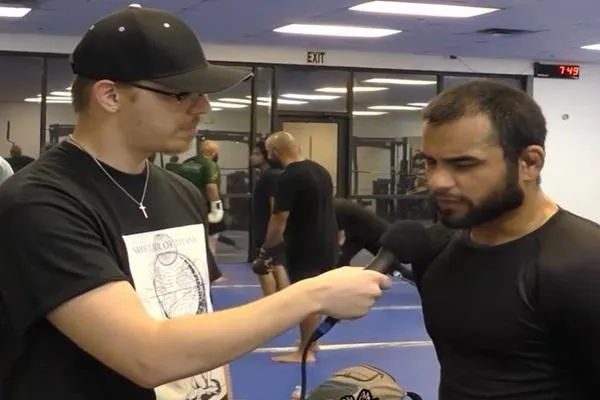 An interviewer holding a microphone while speaking to a fighter inside a gym, highlighting a pre-fight media interaction.