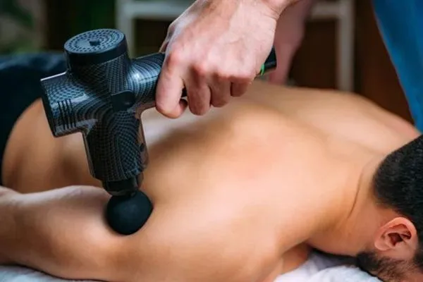 A fighter receiving a massage with a massage gun, highlighting an essential recovery tool for muscle relief and performance enhancement.