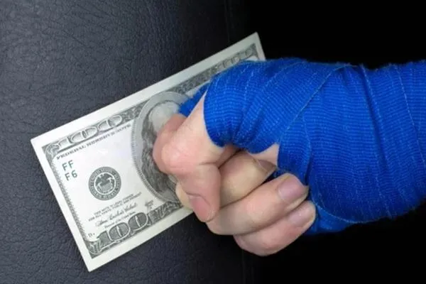 Close-up of a fighter's hand wrapped in blue hand wraps gripping a hundred-dollar bill, symbolizing the financial side of MMA and making money as a fighter.