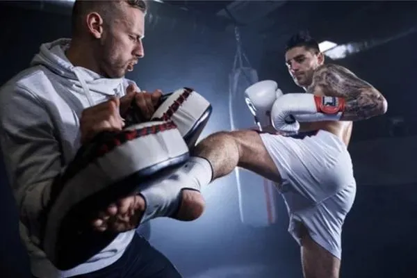 Kickboxer executing a powerful kick on training pads during an intense padwork session.