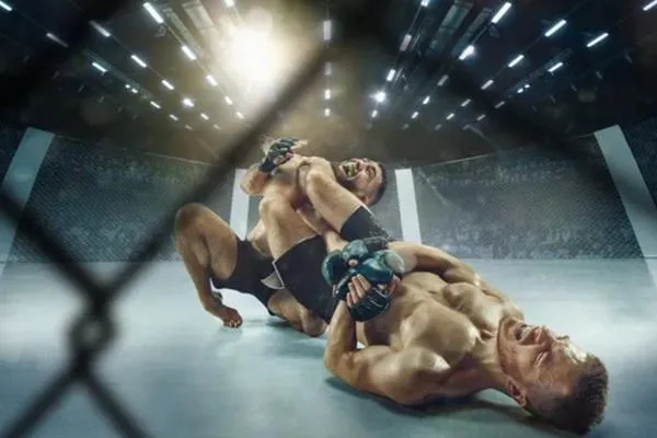 Two MMA fighters demonstrating strength and grappling techniques inside a cage under bright arena lights.