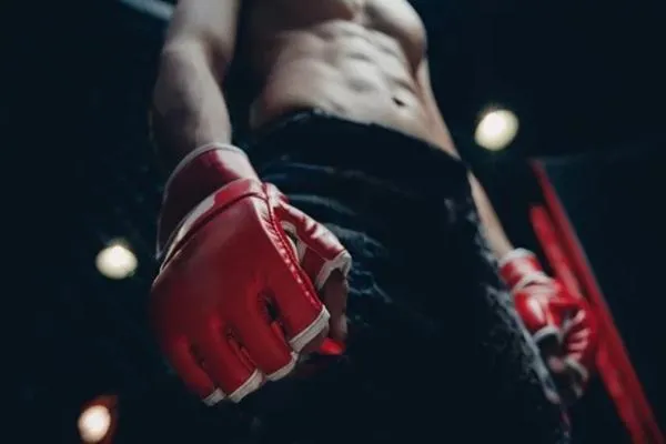 Close-up of an MMA fighter wearing red gloves, standing confidently inside the cage under the arena lights, ready for competition.