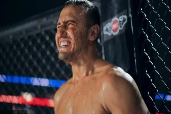 A determined MMA fighter grimaces in pain inside the cage, showcasing the mental and physical endurance required to withstand damage in combat sports.