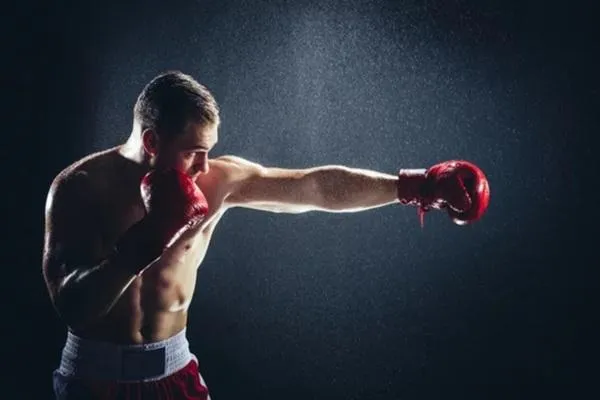 Boxer in red gloves throwing a straight punch in a dark studio setting, representing focused stance training for Southpaw vs. Orthodox matchups.