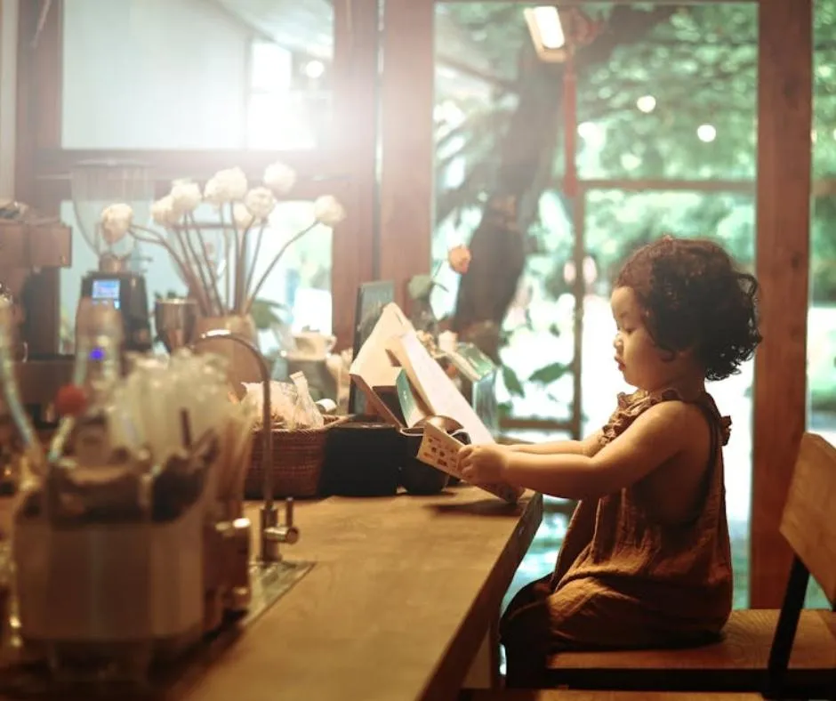 Child sitting at a café table reading a menu, surrounded by a cozy atmosphere with flowers and wooden decor, emphasizing family-friendly dining experiences near Chroma Early Learning Academy.
