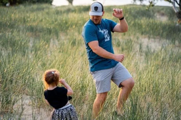 Father dancing playfully with young daughter in grassy field, illustrating the importance of father involvement in child development and emotional health.