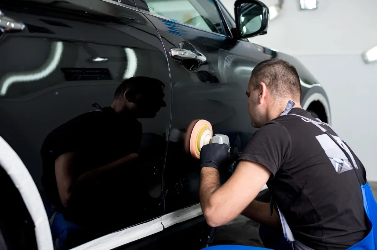 Professional auto detailer performing paint correction on a black vehicle using a dual-action polisher to restore shine and remove imperfections.
