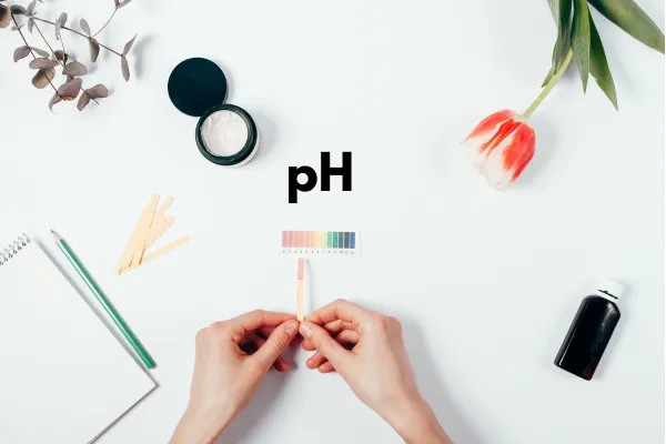 hands holding ph paper with a small container of lotion
