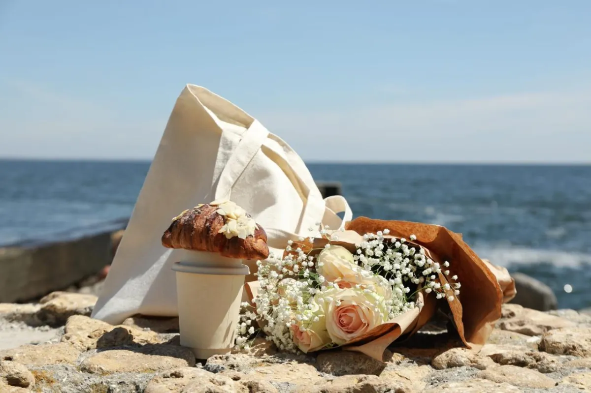 Shores Kitchen Santa Monica- tote bag, flowers, delicious crossiant and hot coffee on beach with ocean background