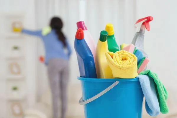 Cleaning supply bucket filled with various cleaners, with a person cleaning in the blurred background