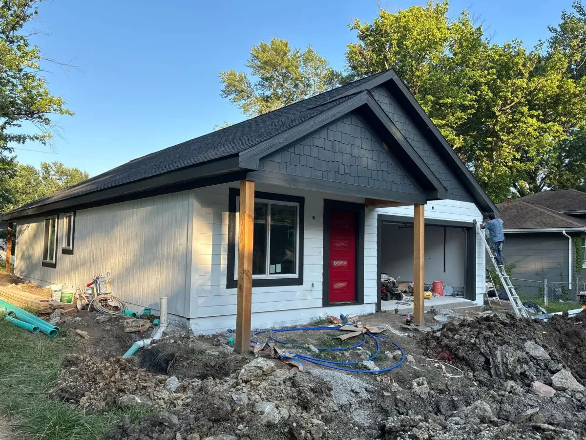 White house with black pitched roof on gravel with red door - new construction