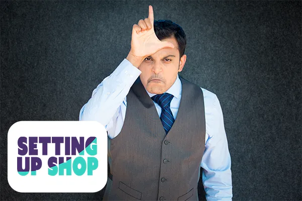 Angry looking business man making an L-shape for loser against his forehead