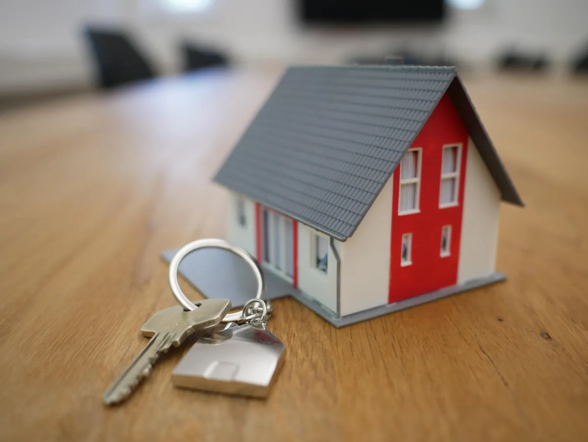 Photo of a small model house with red door and house keys lying next.