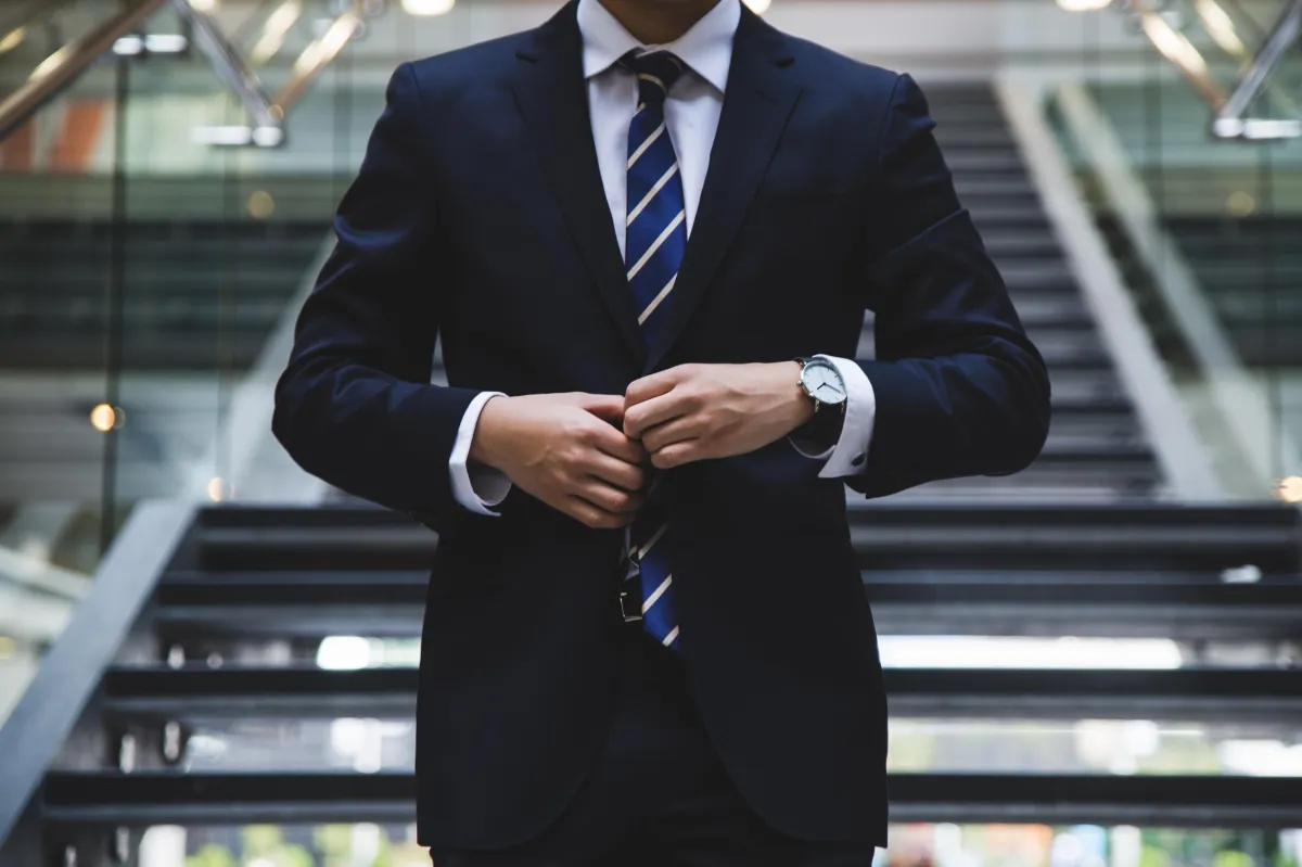 Man dressed in suit, buttoning his middle button on the coat jacket.