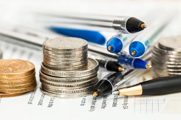 Stack of coins and pens on top of papers