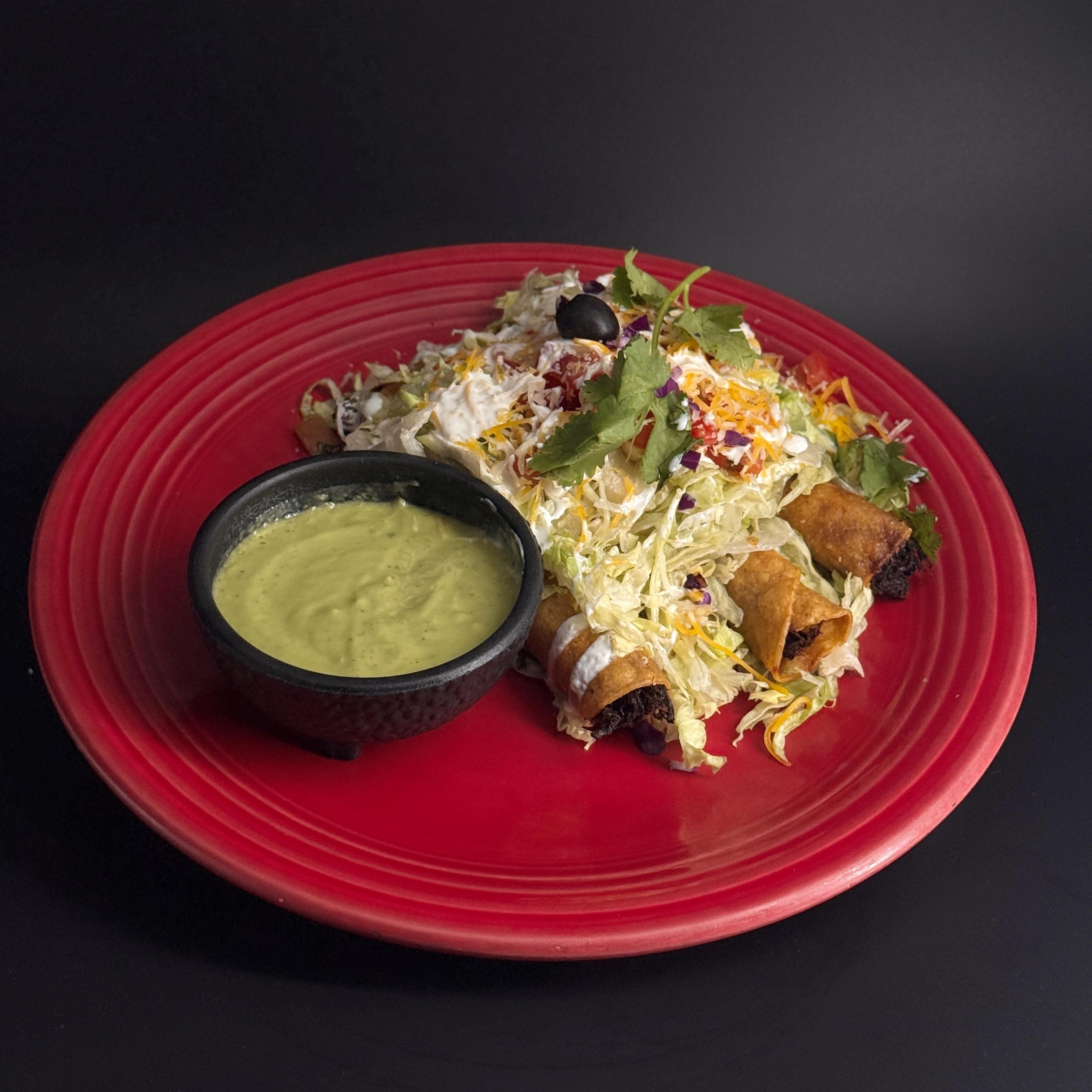 Taquitos Rancheros at Casa de Bandini — four crispy corn tortilla beef taquitos topped with lettuce, tomato, cheese, Mexican crema and spicy avocado salsa in Carlsbad CA