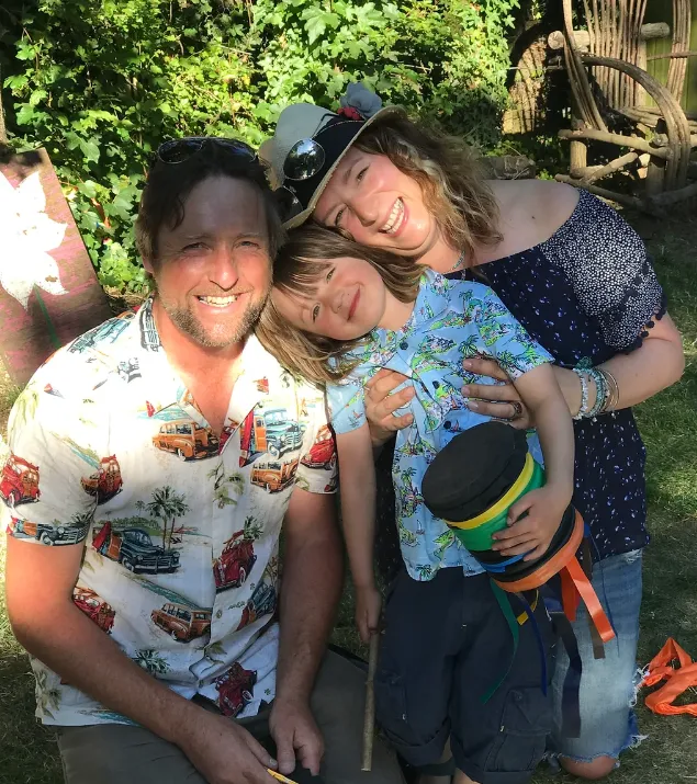 pic of Mark, Rachel and 4 year old H smiling at the camera, standing closely together
