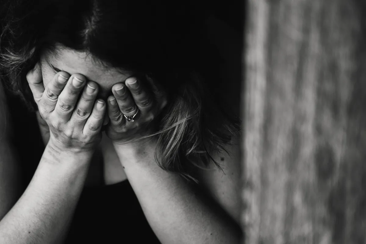 A woman sitting alone in a dimly lit church pew, head bowed in grief, as sunlight filters through stained glass—symbolizing pain and a glimmer of hope