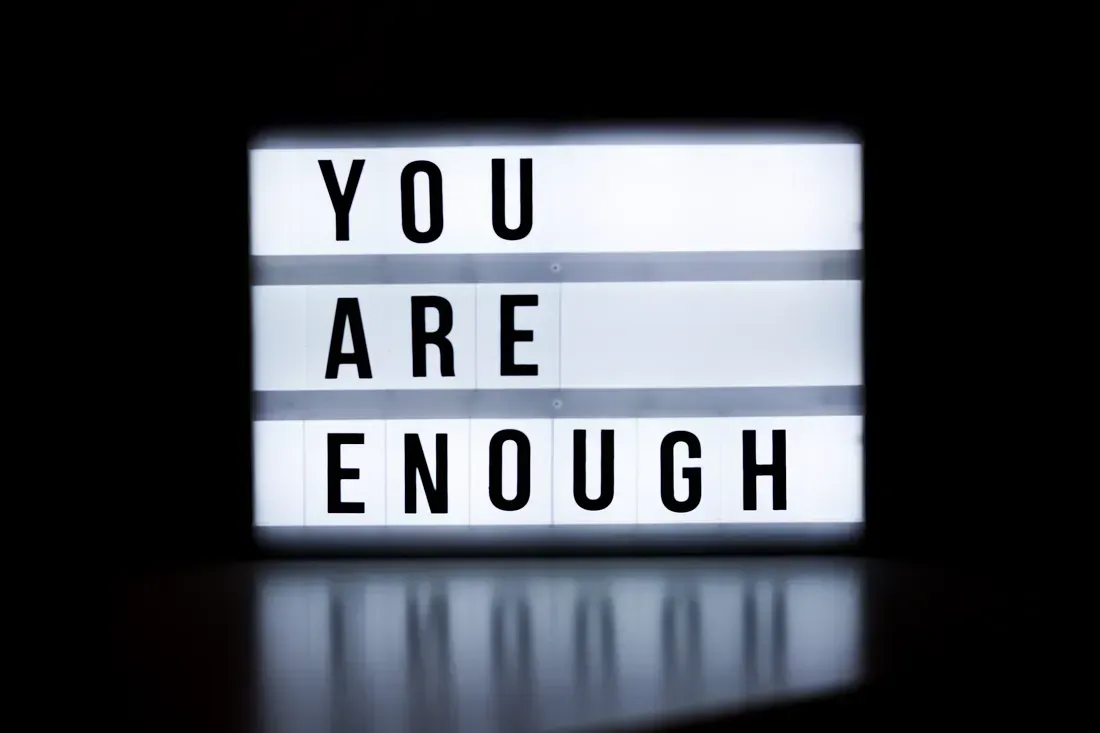 A lightbox sign with bold black letters on a white background displaying the message "YOU ARE ENOUGH" against a dark background.